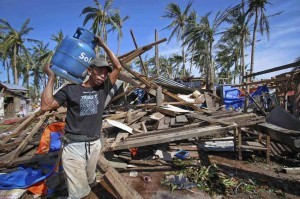 A typhoon victim carries a cooking gas tank past a house destroyed by typhoon Ruby in Borongan, Samar on Monday. More than a million people were evacuated as the powerful typhoon approached the country, fearing a repeat of last year's typhoon that left 7,000 dead or missing. (MNS photo)
