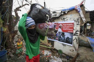 A man carrying bags of used plastic passes by a poster addressed to Pope Francis at a slum area in Quezon City on Tuesday. Millions of Filipinos will gather in Metro Manila and Leyte for the Papal visit, with some of them showing the pontiff how they live. (MNS photo)
